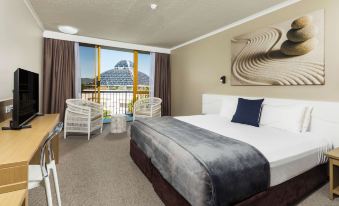 a large bed with a gray blanket is in the middle of a room with chairs and a window at Pacific Hotel Cairns