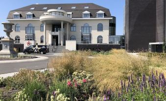 a large white building with a curved roof , surrounded by lush greenery and flowers , under a clear blue sky at Hotel Acropolis