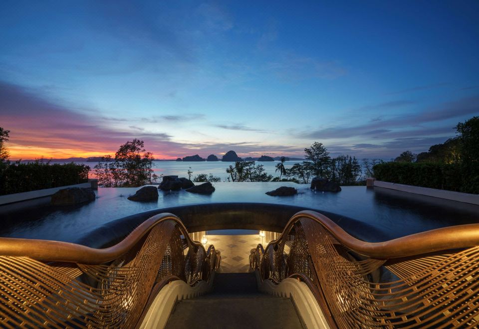 a staircase leading down to a body of water , with the sun setting in the background at Banyan Tree Krabi