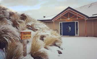 a snow - covered house with a blue door , surrounded by trees and grass , and a sign nearby at Lakestone Lodge