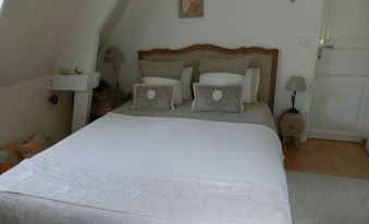 a large bed with a white comforter and gray pillows is in a bedroom with a slanted ceiling at Le Pressoir