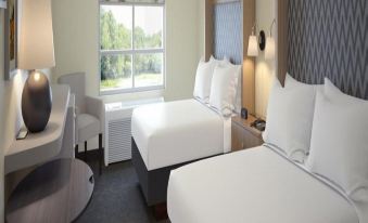 a hotel room with two beds , each made up with white linens and pillows , near a window that overlooks a lake at Holiday Inn & Suites Arden - Asheville Airport
