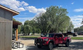 a red pickup truck is parked next to a building , with trees and a blue sky in the background at Challis Roadhouse