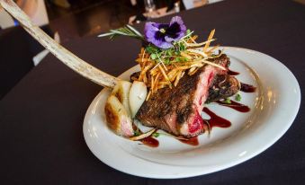 a white plate with a large piece of meat on it , accompanied by a fork and knife at The Mosey Buffalo Williamsville, Tapestry Collection by Hilton