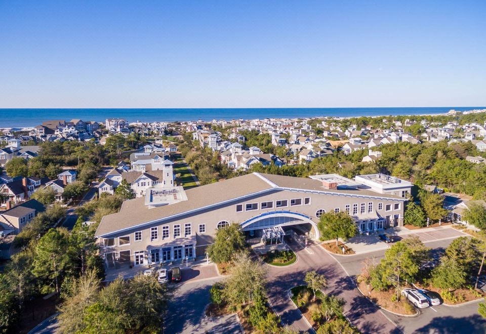 an aerial view of a large building with a white roof and brown trim , surrounded by trees and houses near the ocean at WaterSound Inn