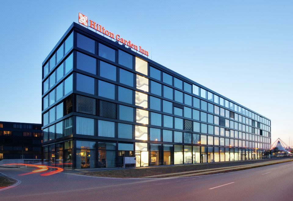 a modern building with a large glass facade and the hilton garden inn logo in red on top at Hilton Garden Inn Zurich Limmattal