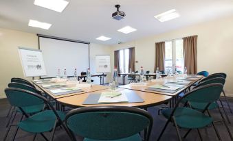 a conference room with a large round table surrounded by chairs and a projector screen at Campanile Rouen Est - Franqueville Saint Pierre