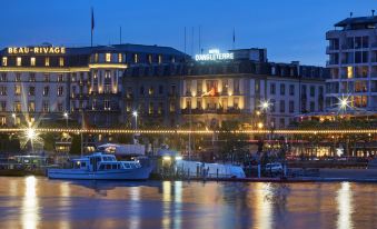 a city skyline at night , with a large building illuminated by lights and a boat on the water at Hotel d'Angleterre