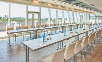 a long dining table set up for a meeting , with chairs arranged around it and a view of the ocean at NH Collection Santiago de Compostela