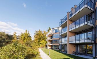 a modern apartment building surrounded by greenery and trees , with a grassy area in front of it at Oaks Queenstown Shores Resort