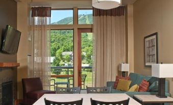 a room with a large window and sliding glass door , featuring colorful pillows and a dining table at Jay Peak Resort