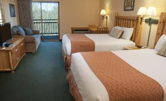 a hotel room with two beds , each made up with white linens and orange blankets , next to a window that overlooks a balcony at The Waters of Minocqua