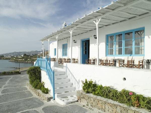 a white building with blue trim , situated on the shore of a body of water at Mykonos Beach Hotel