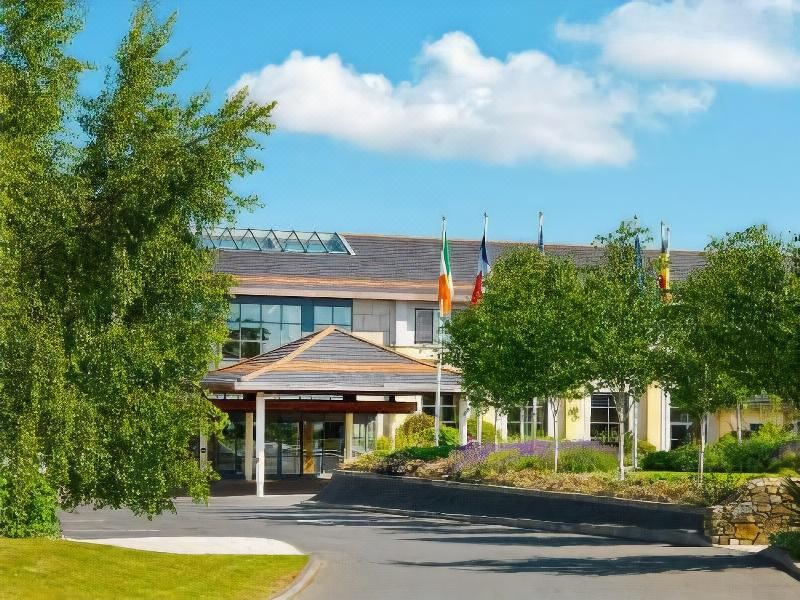 a large hotel building surrounded by trees and grass , with a blue sky in the background at Druids Glen Resort