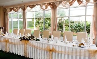 a long table with a gold ribbon and floral centerpiece is set up in front of a window at Majestic Hotel