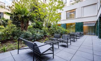 a row of black lounge chairs in front of a building with trees and bushes at NH Collection Antwerp Centre