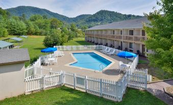 an outdoor swimming pool surrounded by a white picket fence , with umbrellas and chairs placed around the pool area at Americas Best Value Inn Canton