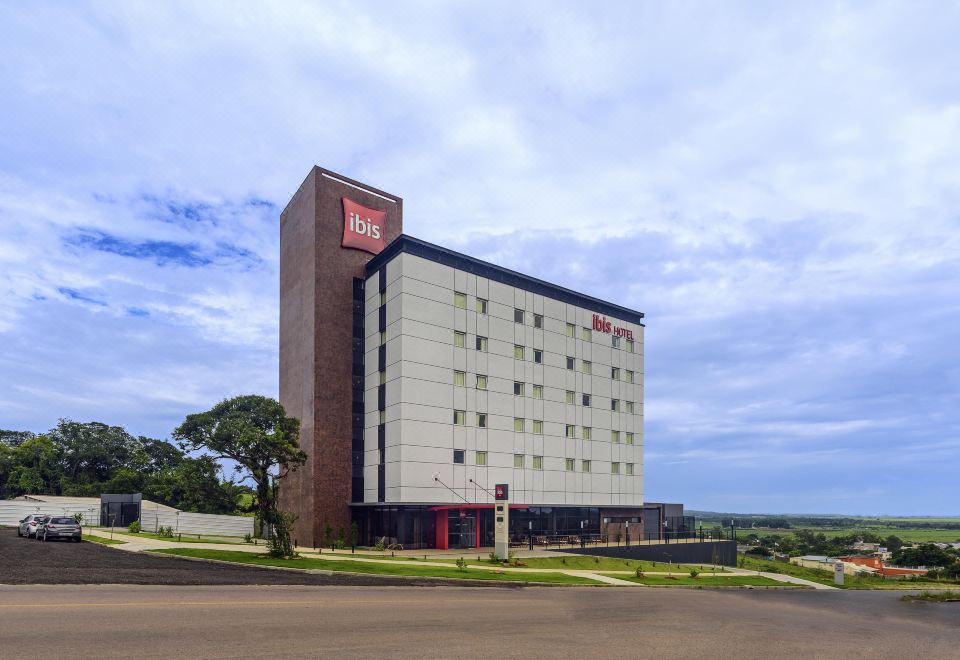 a large hotel building situated on a city street , surrounded by cars and trees , under a cloudy sky at Ibis Guaiba