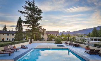 a beautiful outdoor pool area with umbrellas , sun loungers , and a scenic view of houses and mountains , set against a backdrop of clear blue at Hanmer Springs Hotel