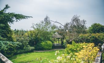 a lush green lawn with a gazebo in the distance , surrounded by trees and bushes at The Grange Hotel Brent Knoll