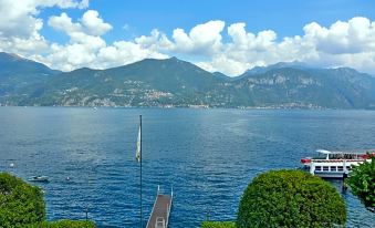 a scenic view of a body of water with mountains in the background and a bench on the shore at Grand Hotel Menaggio