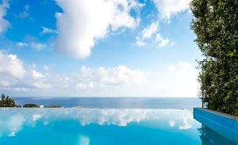 a large swimming pool with blue water and a beautiful view of the ocean , under a cloudy sky at Hotel Ravesi