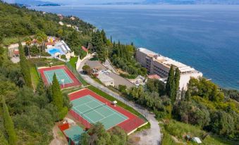 aerial view of a tennis court surrounded by trees and water , with a building in the background at Louis Ionian Sun