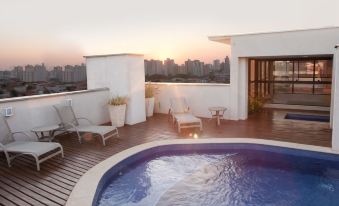 a rooftop with a large swimming pool surrounded by lounge chairs and a city skyline in the background at Ibis Styles Piracicaba