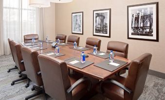 a conference room with a large wooden table , brown leather chairs , and several framed pictures on the wall at Courtyard Houma