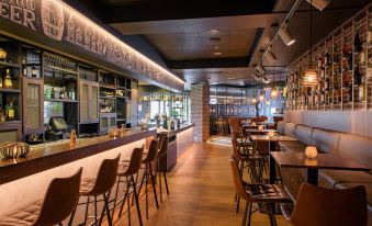 a modern bar with wooden floors , a long bar counter , and several chairs arranged around it at Leonardo Hotel Papendrecht