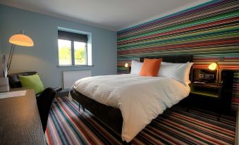 a modern bedroom with a large bed , colorful striped wallpaper , and a window with a view of the outside at Village Hotel Cardiff