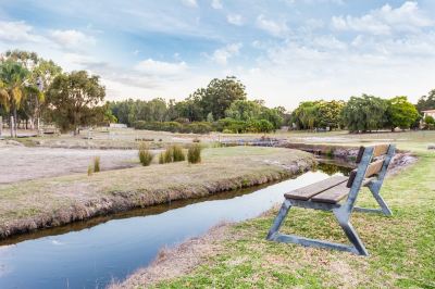 a wooden bench is situated near a river , surrounded by trees and grass , with a clear blue sky overhead at The Swan Valley Retreat