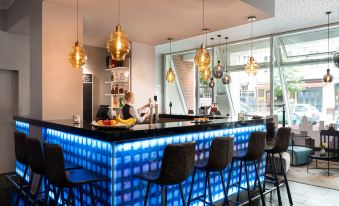a modern bar with a blue and black color scheme , featuring a counter with chairs and pendant lights at Leonardo Hotel Berlin
