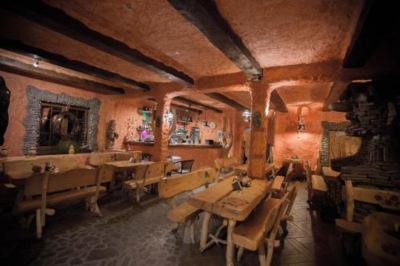 a rustic restaurant with wooden tables and chairs , as well as stone walls and ceiling at Troll