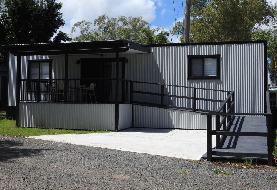 a black and white house with a metal fence , situated on a gravel driveway under a cloudy sky at Lismore Lake Holiday Park