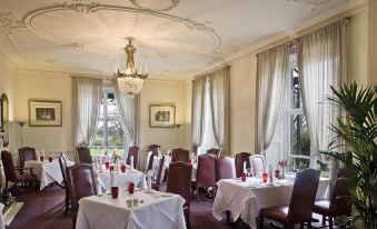 a large , elegant dining room with multiple tables set for a formal dinner , complete with white tablecloths , red cups , and wine at Rookery Hall Hotel & Spa