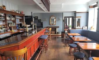 a well - decorated restaurant with wooden tables and chairs , a bar counter , and a blue couch at Blue Bell Hotel