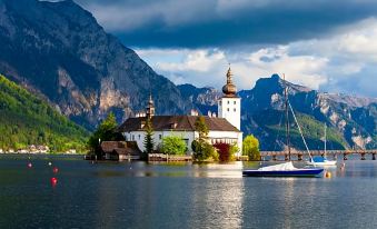 a picturesque view of a lake with a boat floating on the water , surrounded by mountains and a church at Hotel Esplanade