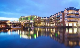 a large building with a green and white sign is reflected in the water at night at Holiday Inn London - Brentford Lock