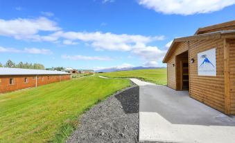 a wooden house surrounded by green grass and a field of yellow flowers , with a clear blue sky above at Hotel Eyjafjallajokull