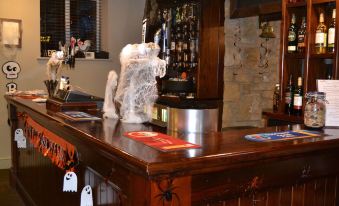 a wooden bar with a bar top covered in ghost and spider decorations , as well as a tv mounted on the wall at Anglers Arms