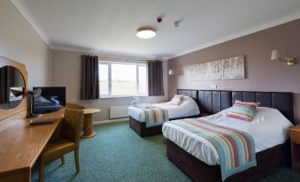 a hotel room with two beds , a window , and a desk , giving a cozy and comfortable atmosphere at Greetham Valley