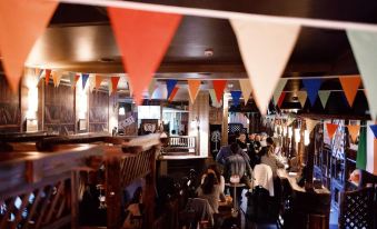 a busy bar with people sitting at tables , tables covered in red and white paper flags hanging from the ceiling , and chairs in the background at Green House