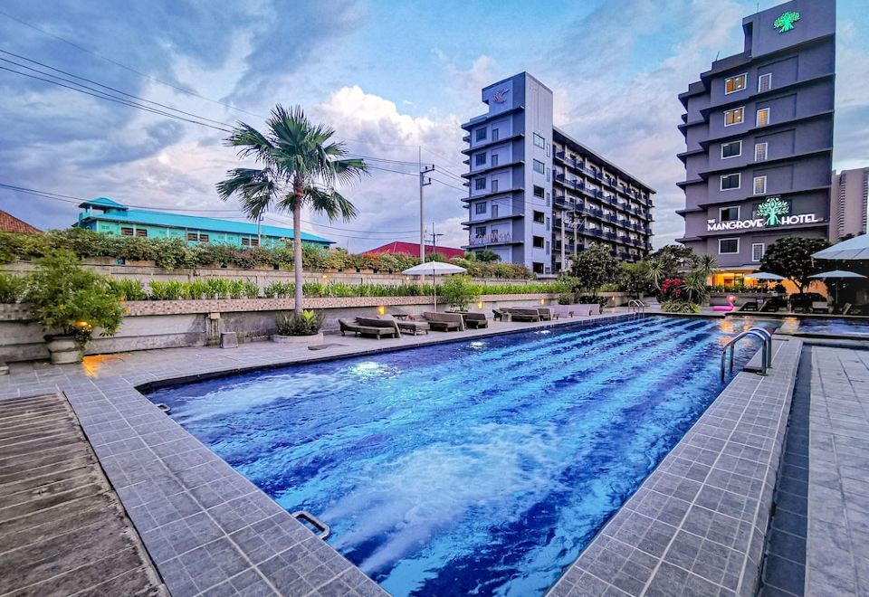 an outdoor swimming pool surrounded by a building , with palm trees in the background at The Mangrove Hotel