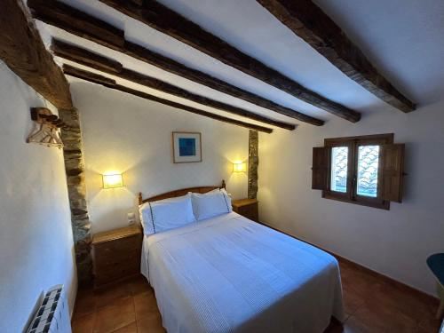 a white bedroom with wooden beams , a bed made up with white sheets , and two lamps on either side of the bed at Apartamentos Turisticos "El Refugio"