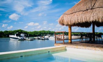 a beach house with a thatched roof overlooks the water , and a swimming pool in the foreground at Villas Grand Marina Kinuh