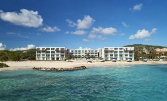 a modern , white apartment building on a sandy beach with clear blue water and white clouds in the sky at Curacao Marriott Beach Resort