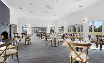 an empty , well - lit dining room with wooden tables and chairs arranged in rows , surrounded by large windows at Sanctuary Inn on Westernport