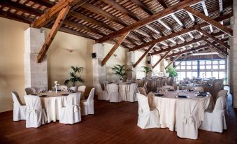 a large room with wooden beams and white walls , featuring several tables and chairs set up for an event at La Tonnara di Bonagia Resort