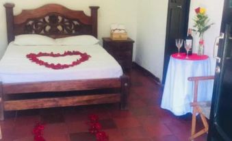 a bedroom with a bed decorated with red rose petals and a wine glass on the table at Hotel San Cristobal